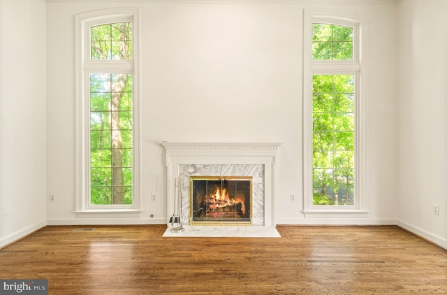unfurnished living room featuring visible vents, a high end fireplace, baseboards, and wood finished floors