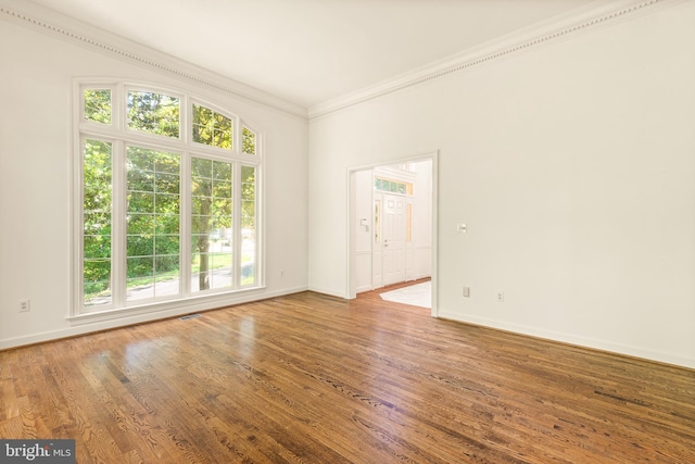 spare room featuring crown molding, baseboards, wood finished floors, and visible vents