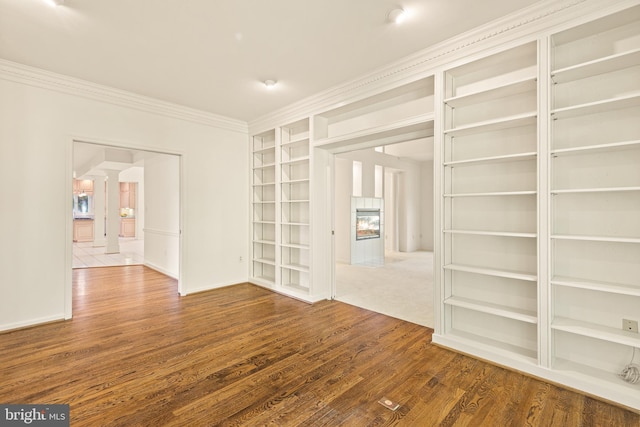unfurnished room featuring crown molding, built in features, baseboards, wood finished floors, and a tile fireplace
