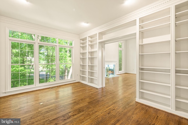 spare room with ornamental molding, built in shelves, wood finished floors, and plenty of natural light