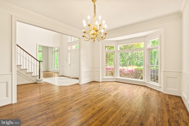 entryway featuring wood finished floors, ornamental molding, a decorative wall, and a notable chandelier