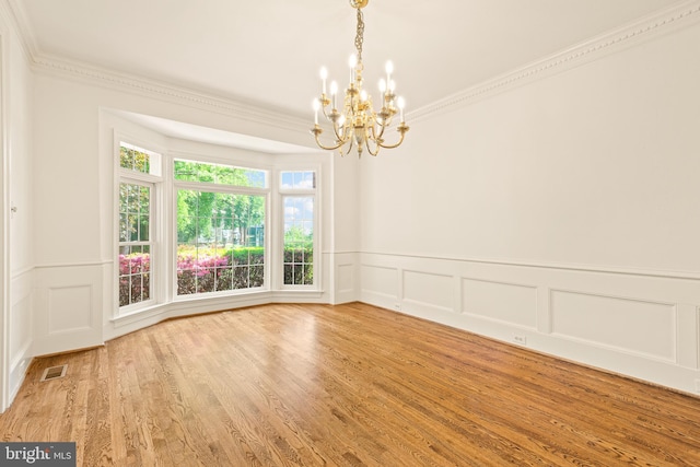 empty room with crown molding, a decorative wall, wood finished floors, and a notable chandelier