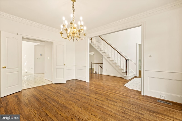 unfurnished dining area with visible vents, crown molding, wood finished floors, an inviting chandelier, and stairs