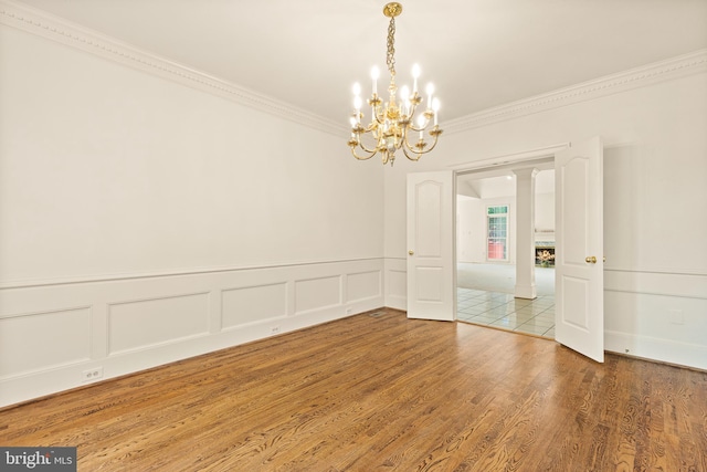 empty room with an inviting chandelier, crown molding, a decorative wall, wood finished floors, and a wainscoted wall