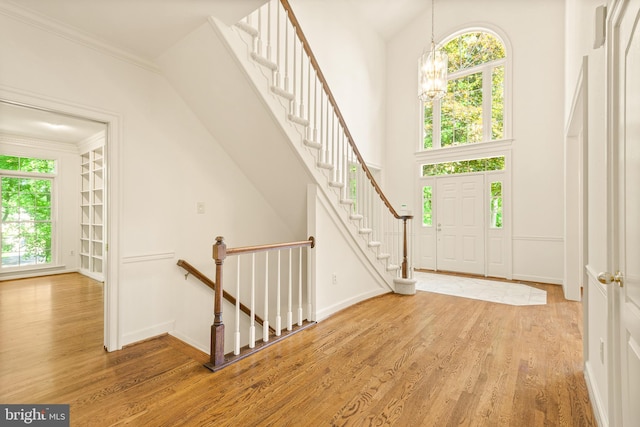 foyer entrance featuring crown molding, baseboards, light wood finished floors, a notable chandelier, and a high ceiling
