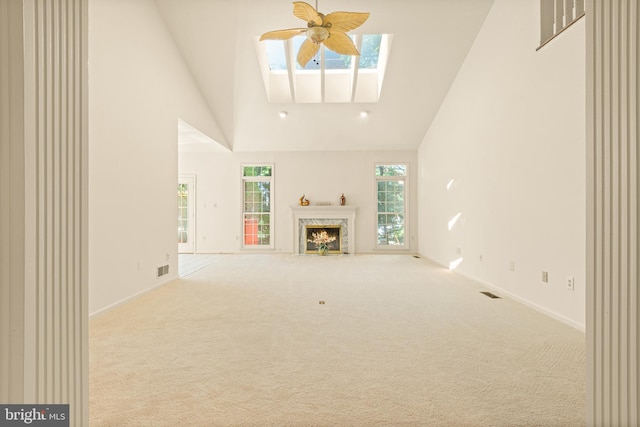 unfurnished living room featuring a skylight, a high end fireplace, high vaulted ceiling, carpet flooring, and baseboards