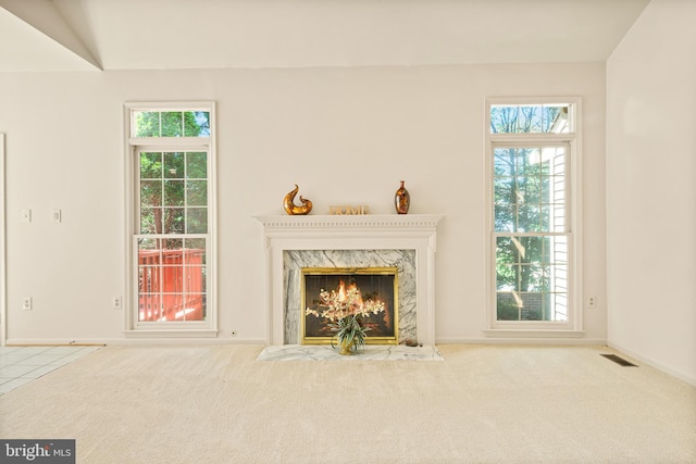 unfurnished living room featuring a premium fireplace, carpet, baseboards, and visible vents