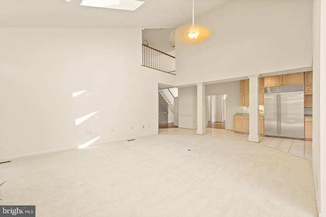 unfurnished living room featuring a sink, high vaulted ceiling, a skylight, stairway, and light colored carpet