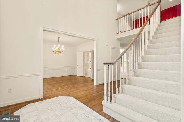 foyer entrance featuring an inviting chandelier, stairs, wood finished floors, a towering ceiling, and ornamental molding