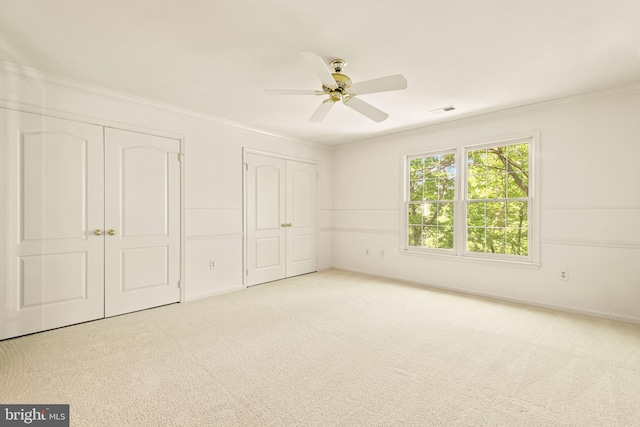 unfurnished bedroom featuring ornamental molding, carpet flooring, multiple closets, and visible vents