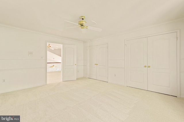 unfurnished bedroom featuring a ceiling fan, multiple closets, crown molding, and carpet