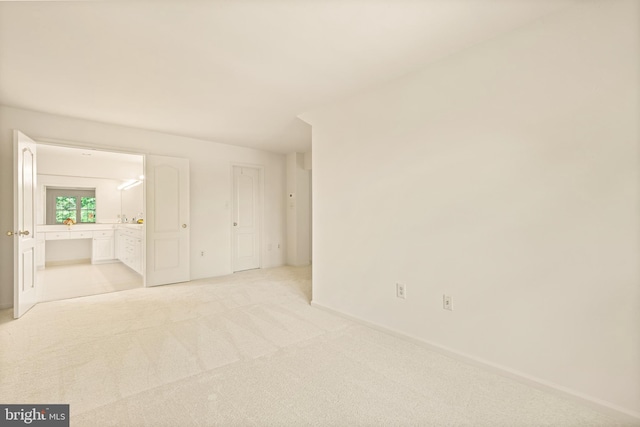 unfurnished bedroom featuring light colored carpet, ensuite bathroom, and baseboards