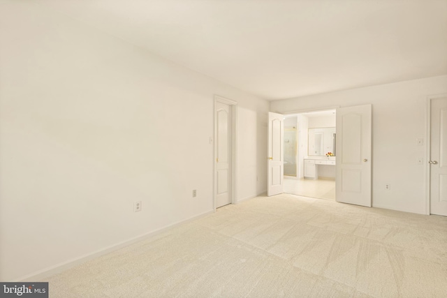 unfurnished bedroom featuring light carpet, ensuite bath, and baseboards