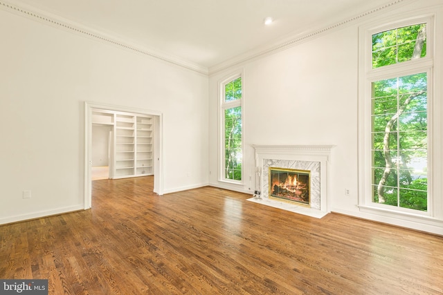 unfurnished living room featuring a fireplace, built in features, baseboards, wood finished floors, and ornamental molding