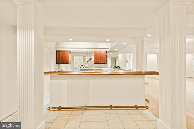kitchen with a tray ceiling, brown cabinetry, decorative columns, light tile patterned flooring, and recessed lighting