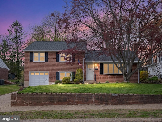 tri-level home with a garage, brick siding, a front yard, and central air condition unit
