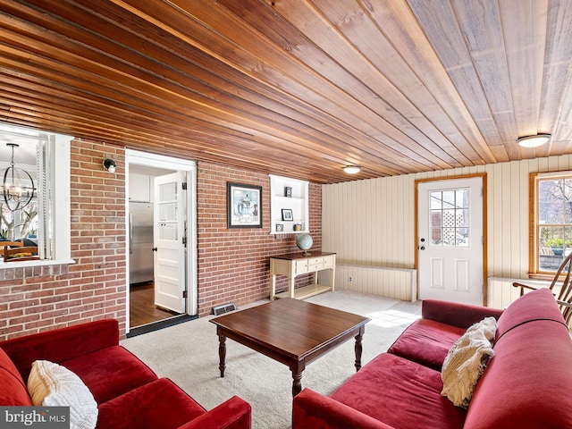 living area with wooden ceiling, brick wall, an inviting chandelier, and carpet flooring