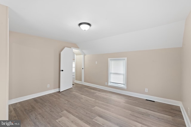 additional living space with baseboards, vaulted ceiling, wood finished floors, and visible vents