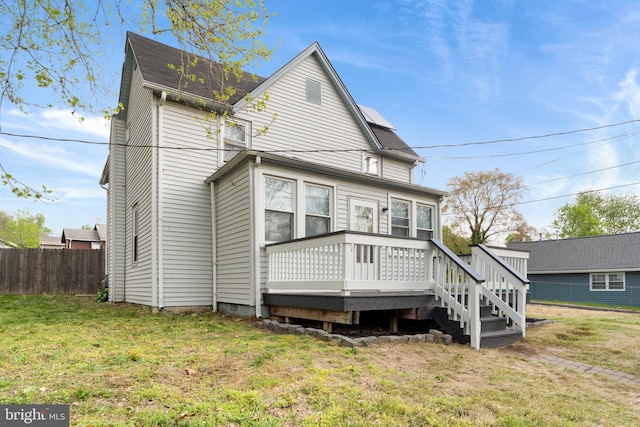 rear view of property featuring a wooden deck, a yard, and fence