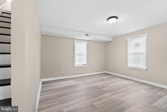 unfurnished room featuring baseboards, wood finished floors, visible vents, and stairway