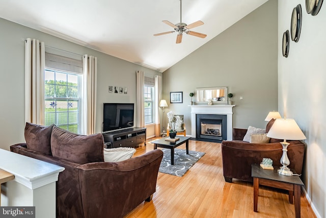 living area with a fireplace, ceiling fan, high vaulted ceiling, and light wood-style floors