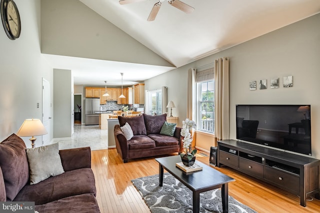 living area with baseboards, light wood-style flooring, ceiling fan, and high vaulted ceiling