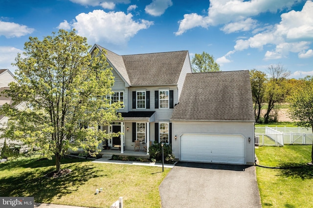 traditional home with covered porch, driveway, a front yard, fence, and a shingled roof