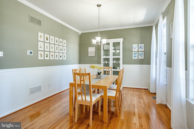 dining room with crown molding, a notable chandelier, visible vents, and hardwood / wood-style floors