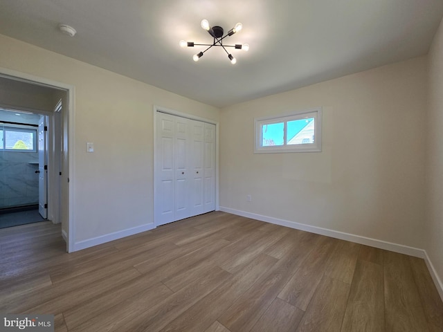 unfurnished bedroom featuring baseboards, wood finished floors, a notable chandelier, and multiple windows