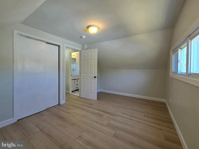 unfurnished bedroom featuring lofted ceiling, a closet, baseboards, and light wood-style flooring