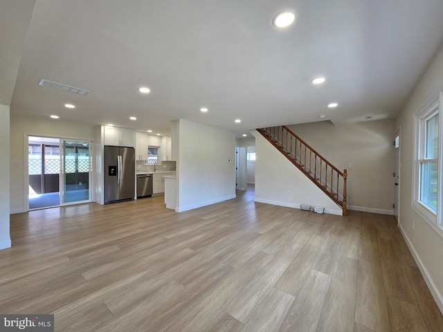 unfurnished living room featuring baseboards, a wealth of natural light, recessed lighting, and stairway