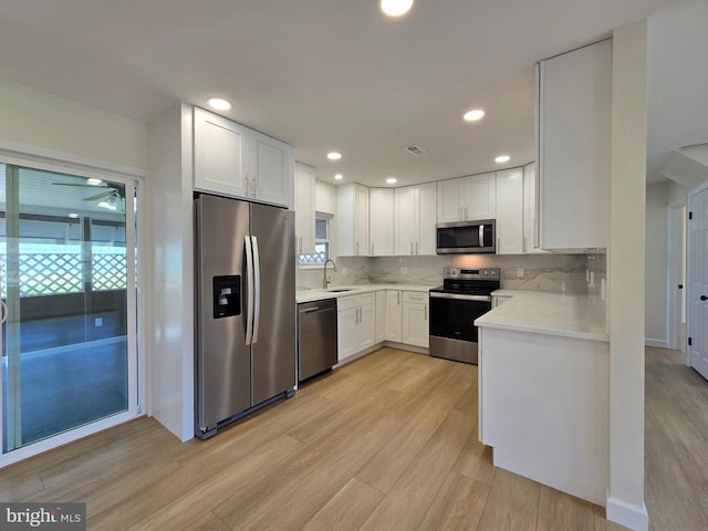 kitchen featuring a sink, light wood-style flooring, light countertops, white cabinets, and appliances with stainless steel finishes