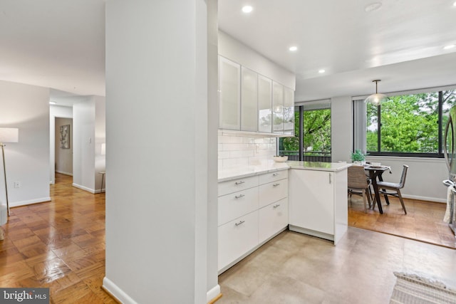 kitchen featuring baseboards, backsplash, a peninsula, and white cabinetry