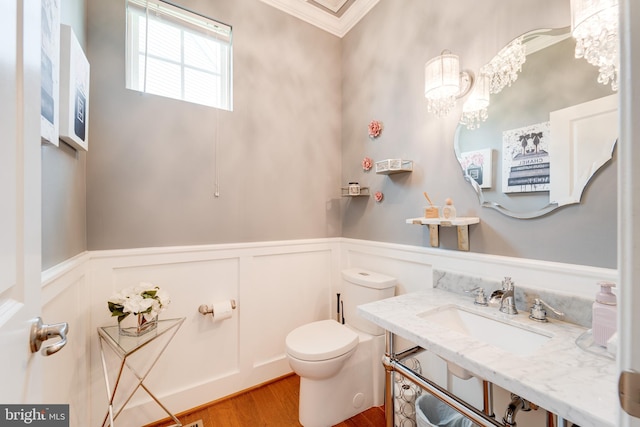 bathroom with a sink, toilet, a wainscoted wall, wood finished floors, and ornamental molding