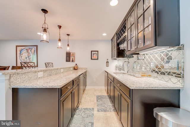 kitchen featuring a peninsula, backsplash, light stone counters, and a sink