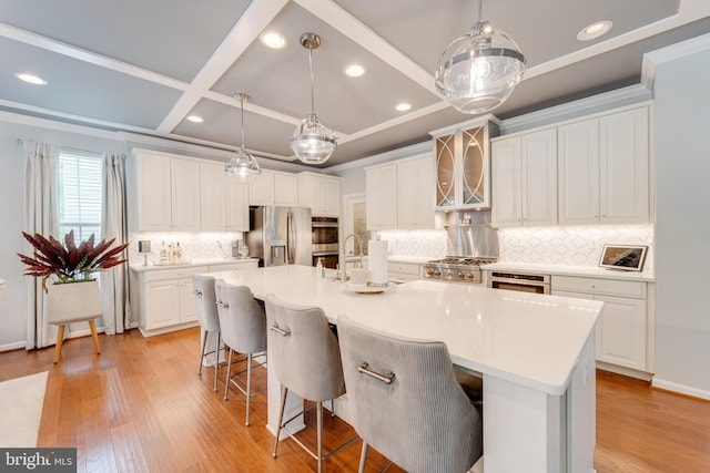 kitchen with light wood-style flooring, a breakfast bar, stainless steel appliances, white cabinets, and decorative backsplash