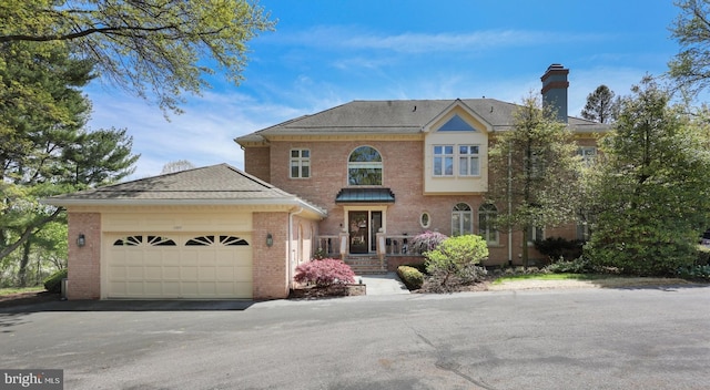 view of front of home featuring brick siding, a garage, driveway, and a chimney