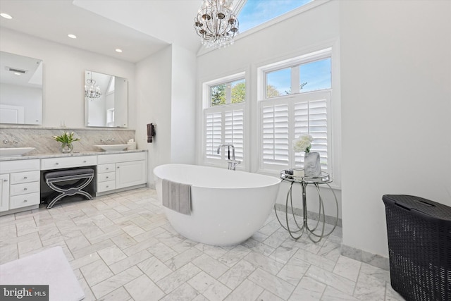 full bath with double vanity, marble finish floor, a soaking tub, a sink, and a notable chandelier