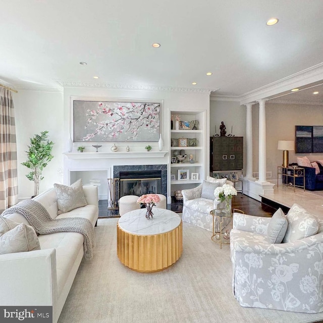 living area featuring crown molding, a premium fireplace, built in features, recessed lighting, and ornate columns