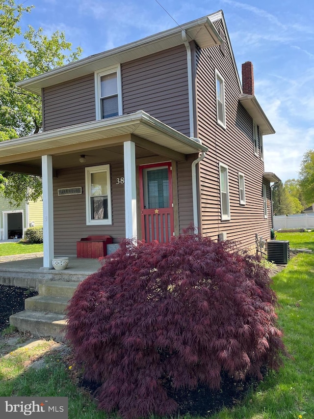 view of front facade with central air condition unit, a chimney, and covered porch