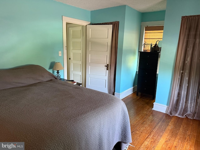 bedroom with wood finished floors, a textured ceiling, and baseboards