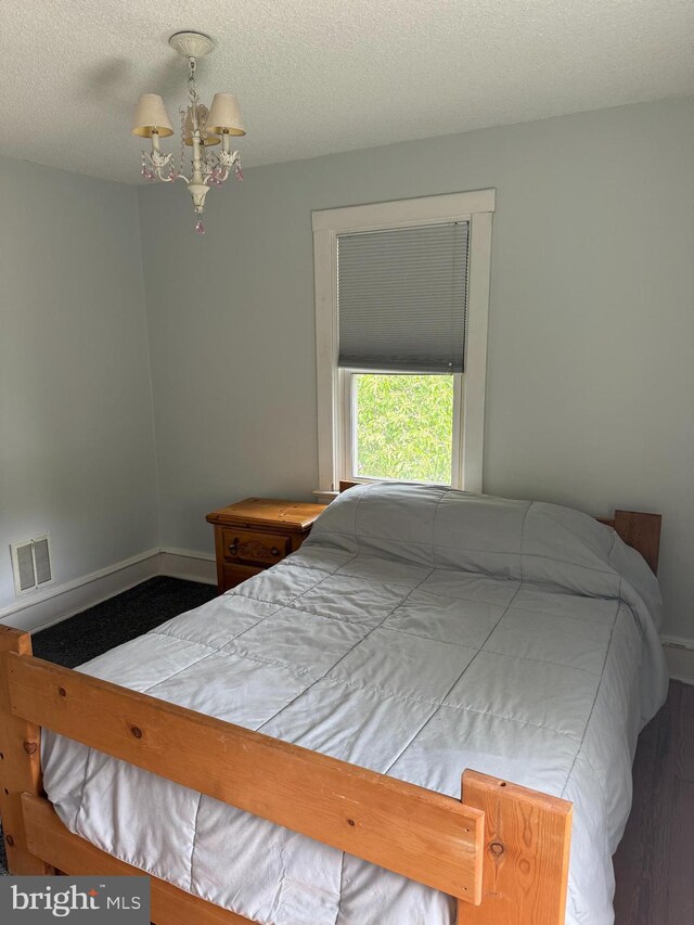 bedroom with an inviting chandelier, wood finished floors, visible vents, baseboards, and a textured ceiling