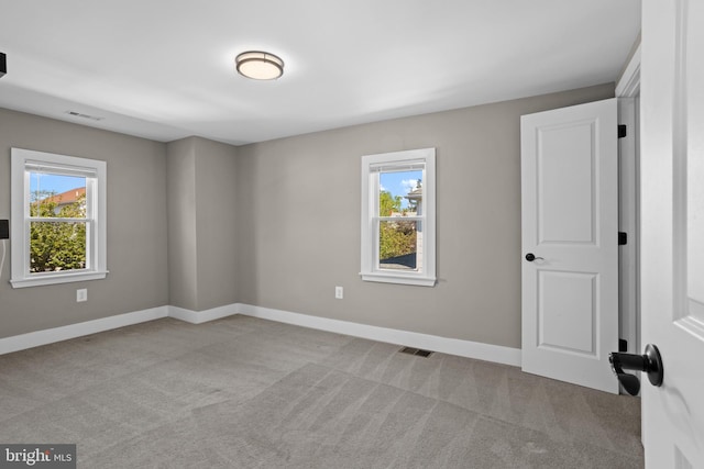 carpeted empty room featuring visible vents, baseboards, and a healthy amount of sunlight