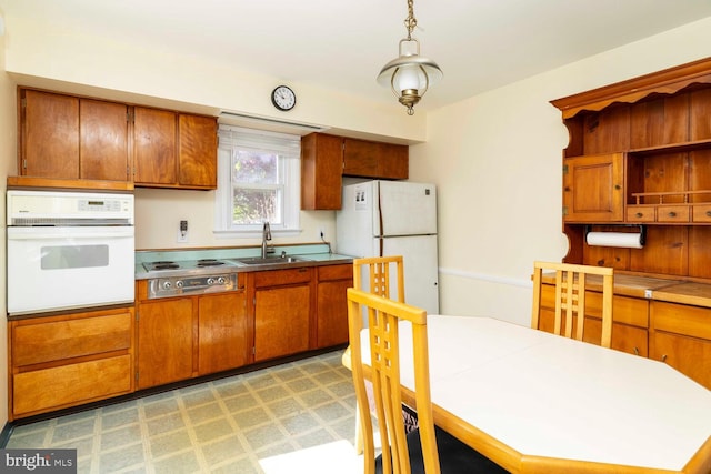 kitchen featuring brown cabinetry, a sink, pendant lighting, and white appliances
