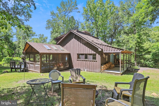 rear view of property featuring roof with shingles, a wooden deck, board and batten siding, a sunroom, and a lawn