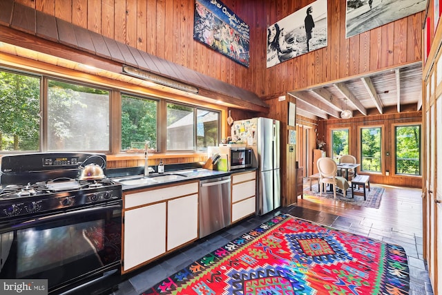 kitchen with a sink, white cabinetry, wooden walls, and stainless steel appliances
