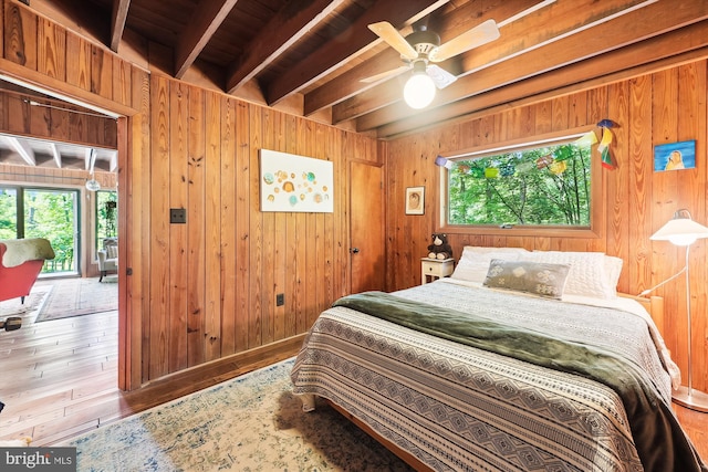 bedroom with multiple windows, beamed ceiling, and wood walls