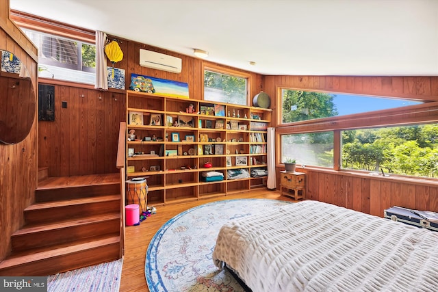 bedroom featuring multiple windows, a wall unit AC, and wood walls