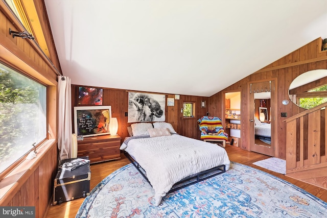 bedroom featuring light wood-style floors, wood walls, and lofted ceiling
