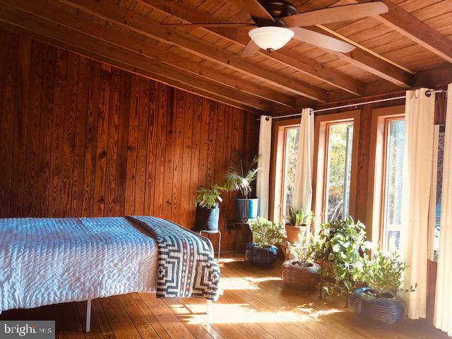 bedroom with wooden walls, lofted ceiling with beams, wooden ceiling, and hardwood / wood-style flooring